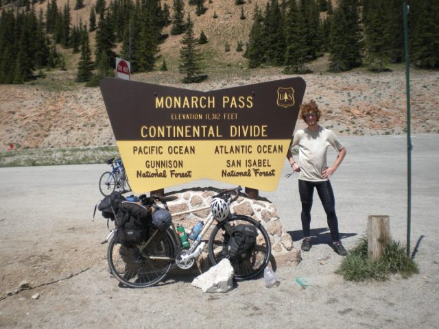 Michael Altfield stands in front of a sign that reads "Monarch Pass Elevation 11,312 feet. Continental Divide." in Colorado, USA