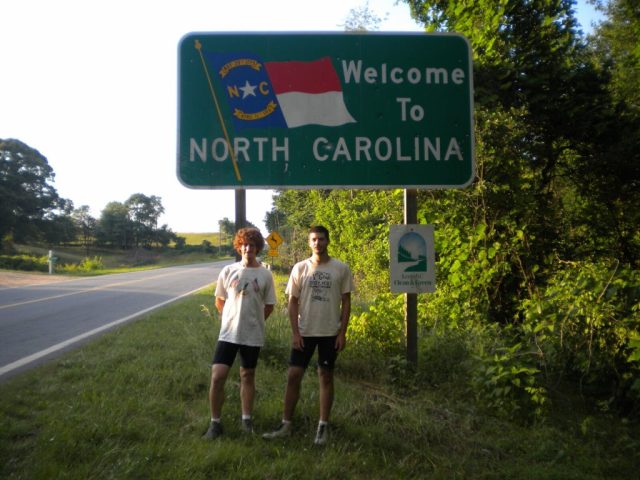 Michael Altfield and Quinn Chrzan stand in-front of a sign that reads "Welcome To North Carolina" in USA