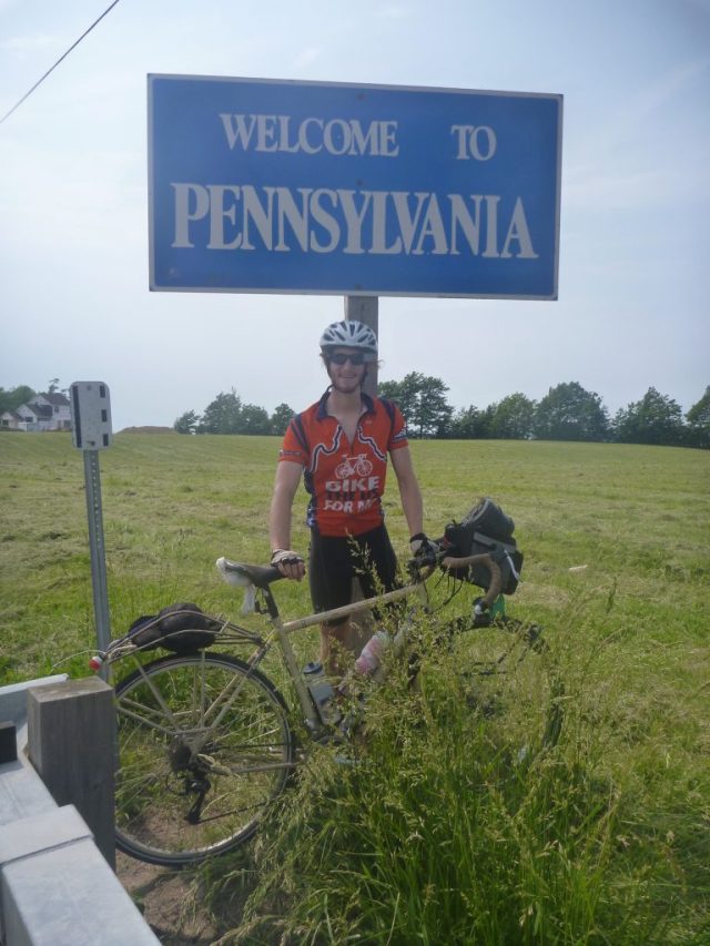 Michael Altfield stands under a sign that says "Welcome To Pennsylvania" in USA