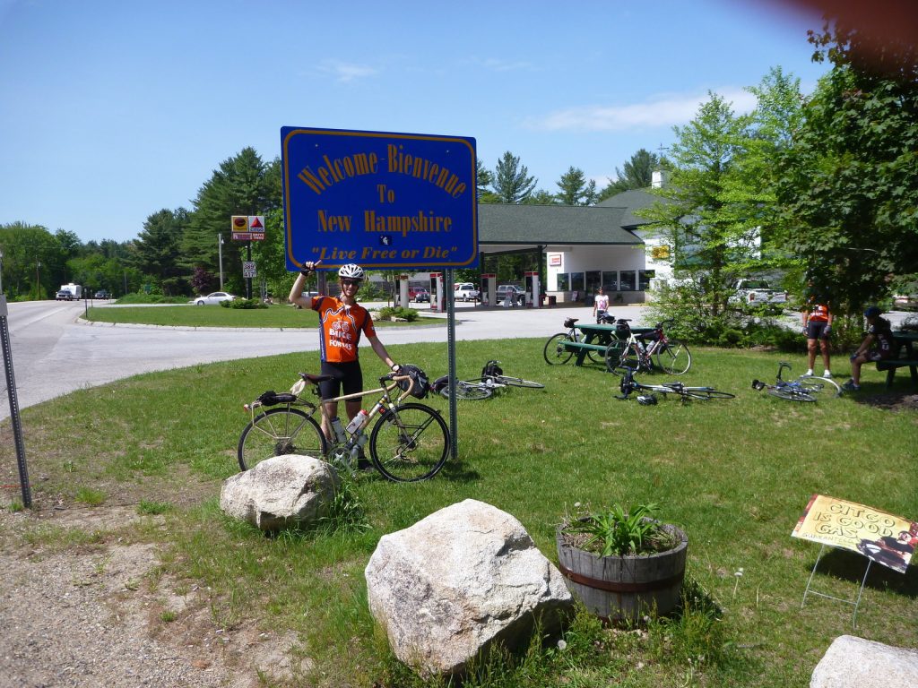 Michael Altfield stands in-front of a sign that reads "Welcome Bienvenne to New Hampshire Live Free or Die" in USA