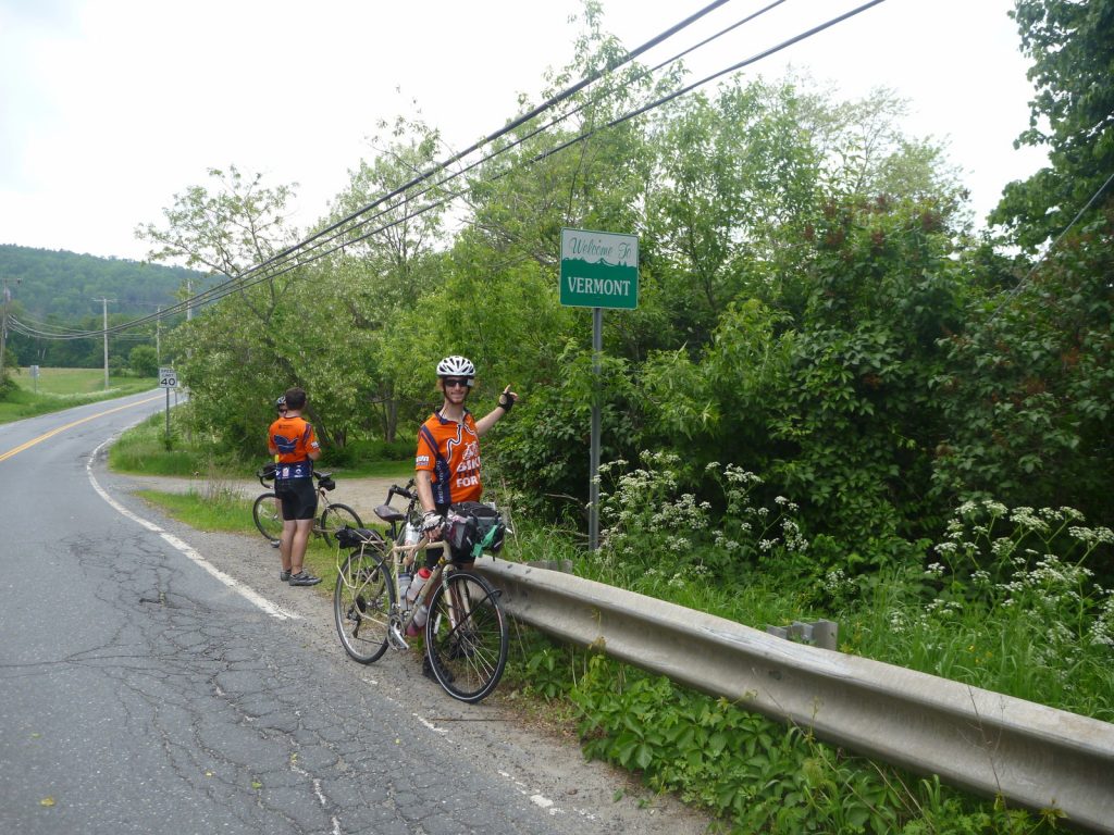 Michael Altfield points to a sign that says "Welcome to Vermont" in USA