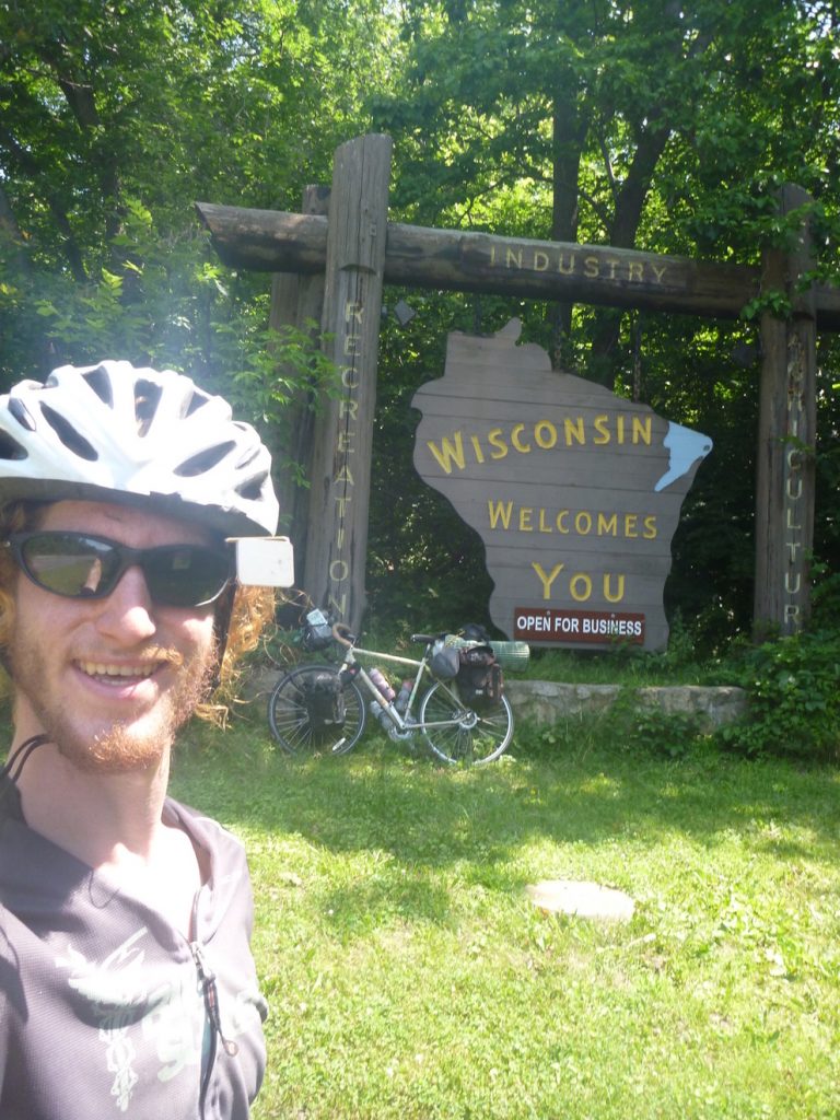 Michael Altfield stands in-front of a sign that says "Wisconsin Welcomes You"